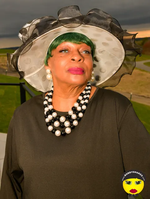 Guest in a black-and-white hat and pearl necklace